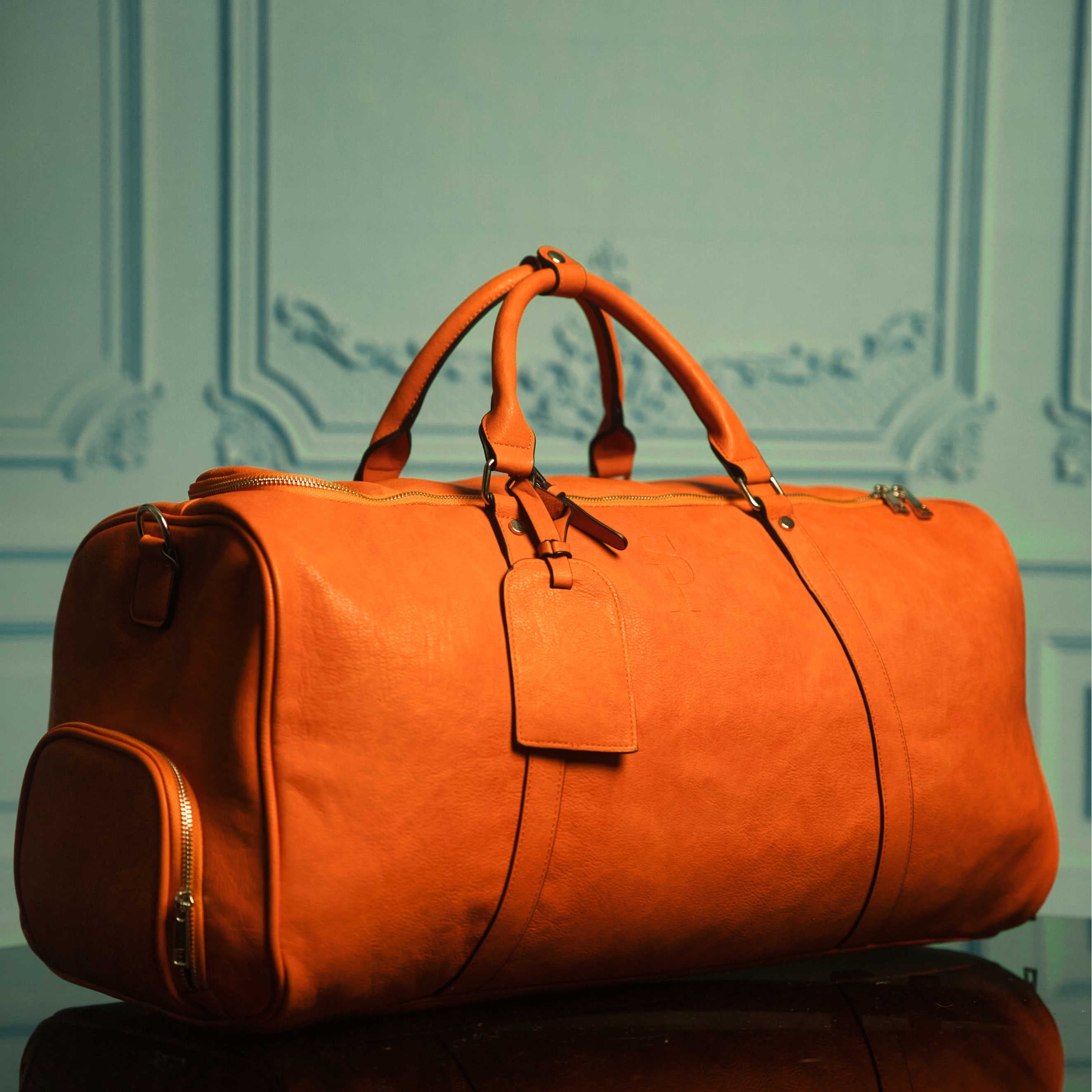 Orange duffel bag on a reflective surface with a patterned wall in the background