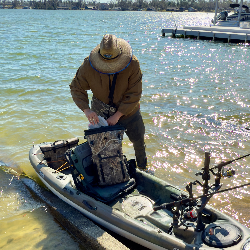 Person preparing a kayak on a body of water with a dock in the background
