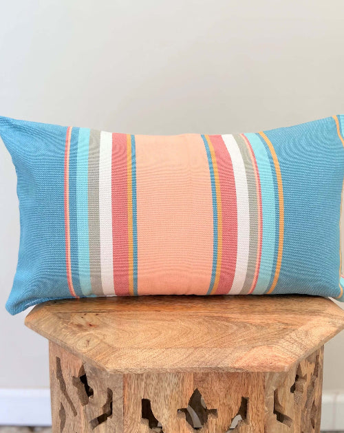 Colorful striped pillow on a wooden stool against a white wall