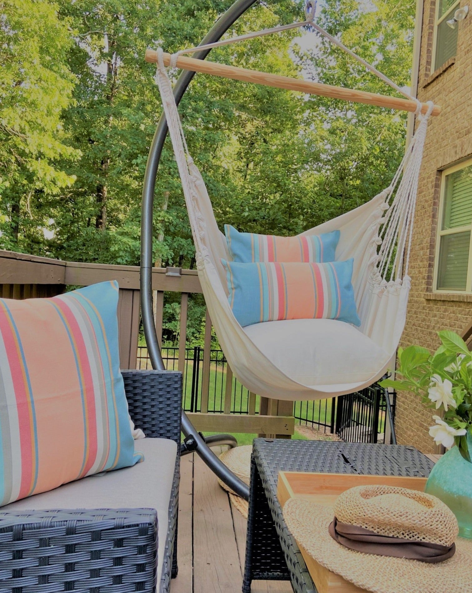 Hanging chair with colorful pillows on a patio with trees and building in the background