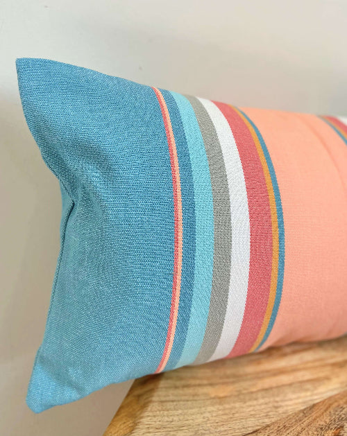 Striped pillow with blue, pink, gray, and white colors on a wooden surface.
