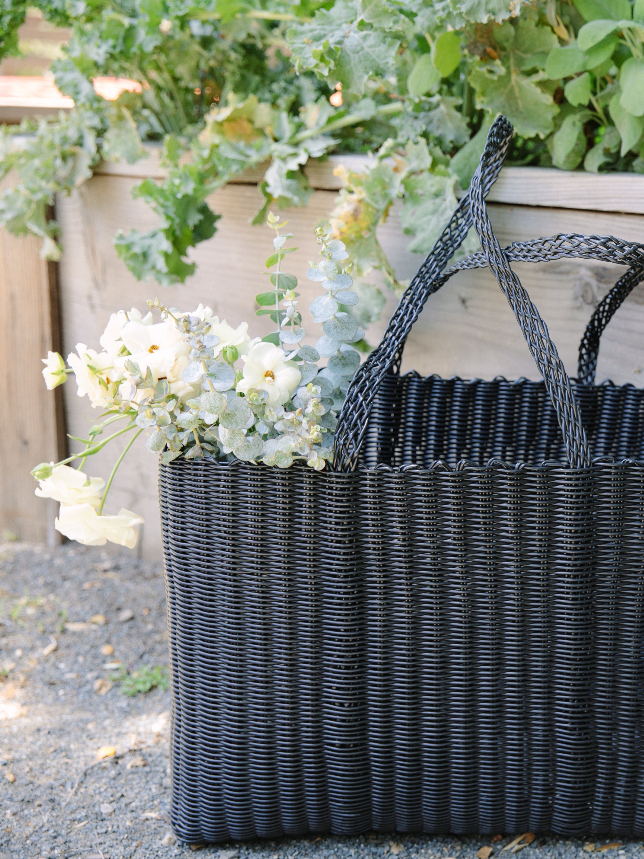 Black woven basket with flowers against a garden background