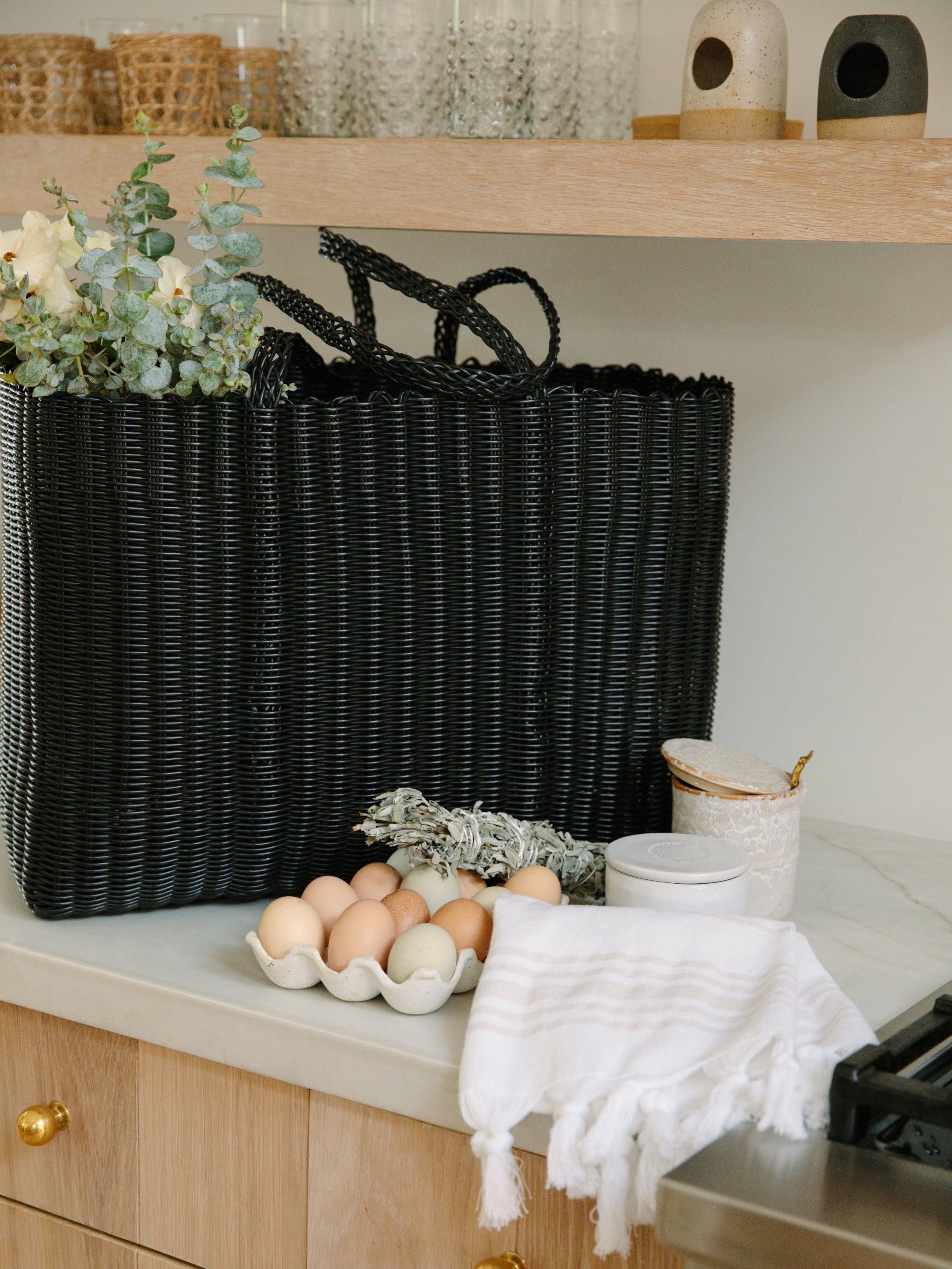 Black woven basket on a kitchen counter with eggs and a white towel.