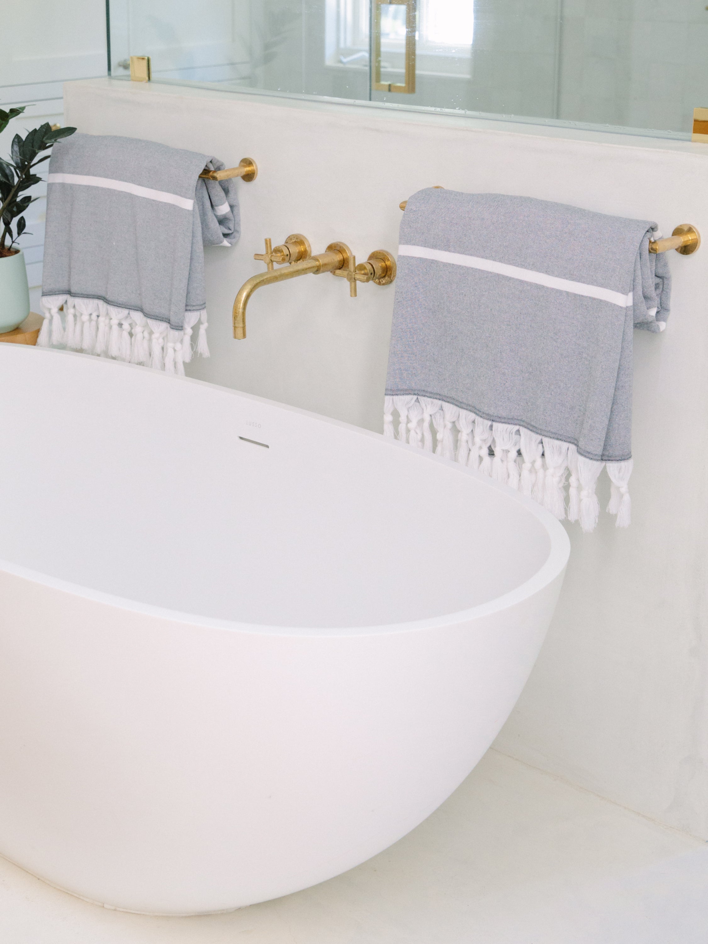 Gray towels with white stripes hanging on gold towel racks above a white bathtub.