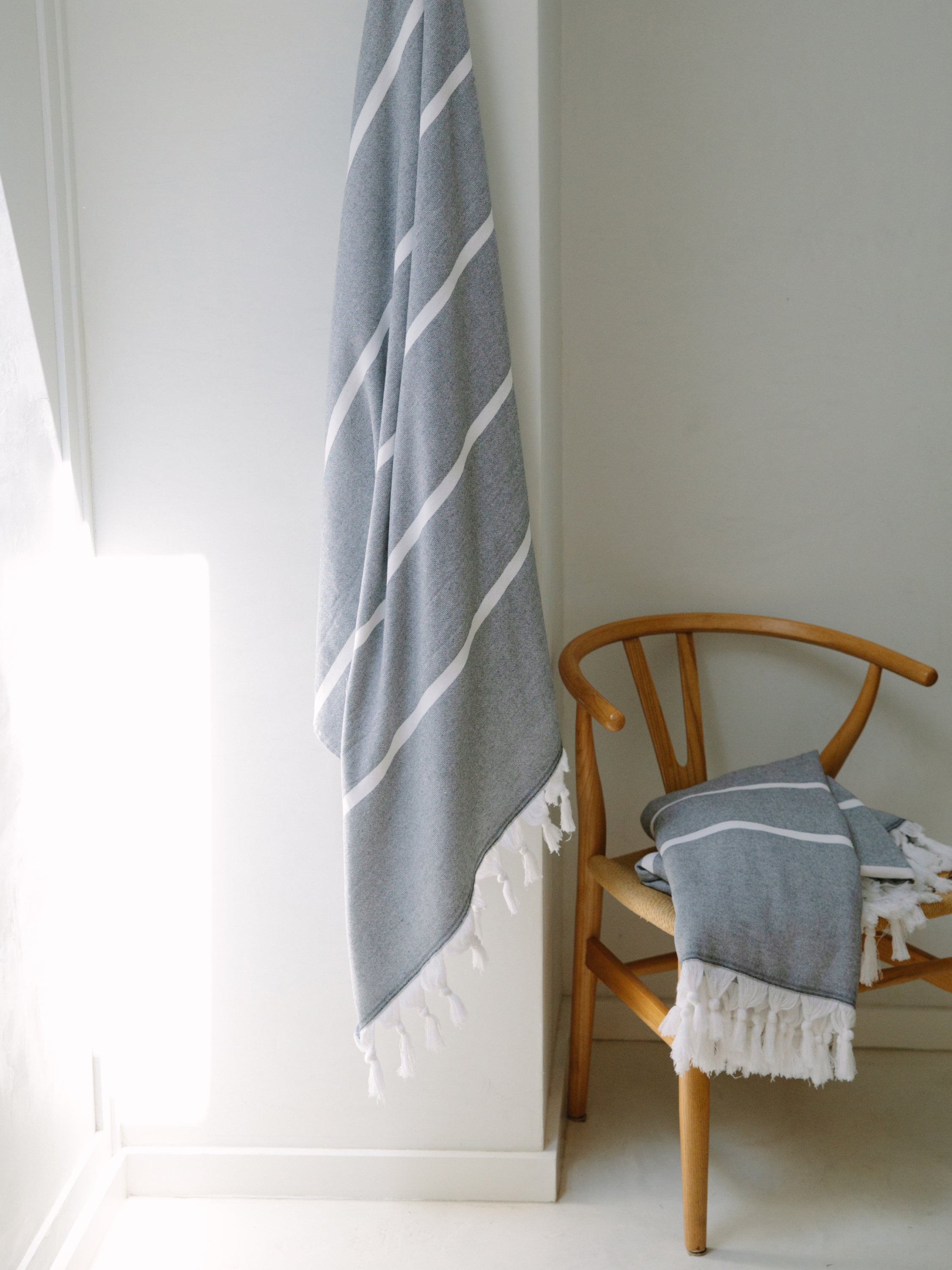 Gray striped towel draped over a wooden chair against a white wall.