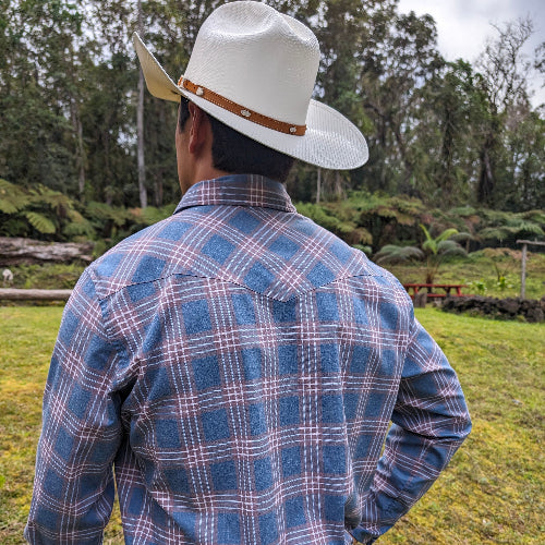 Person wearing a blue plaid shirt and white cowboy hat in a natural setting