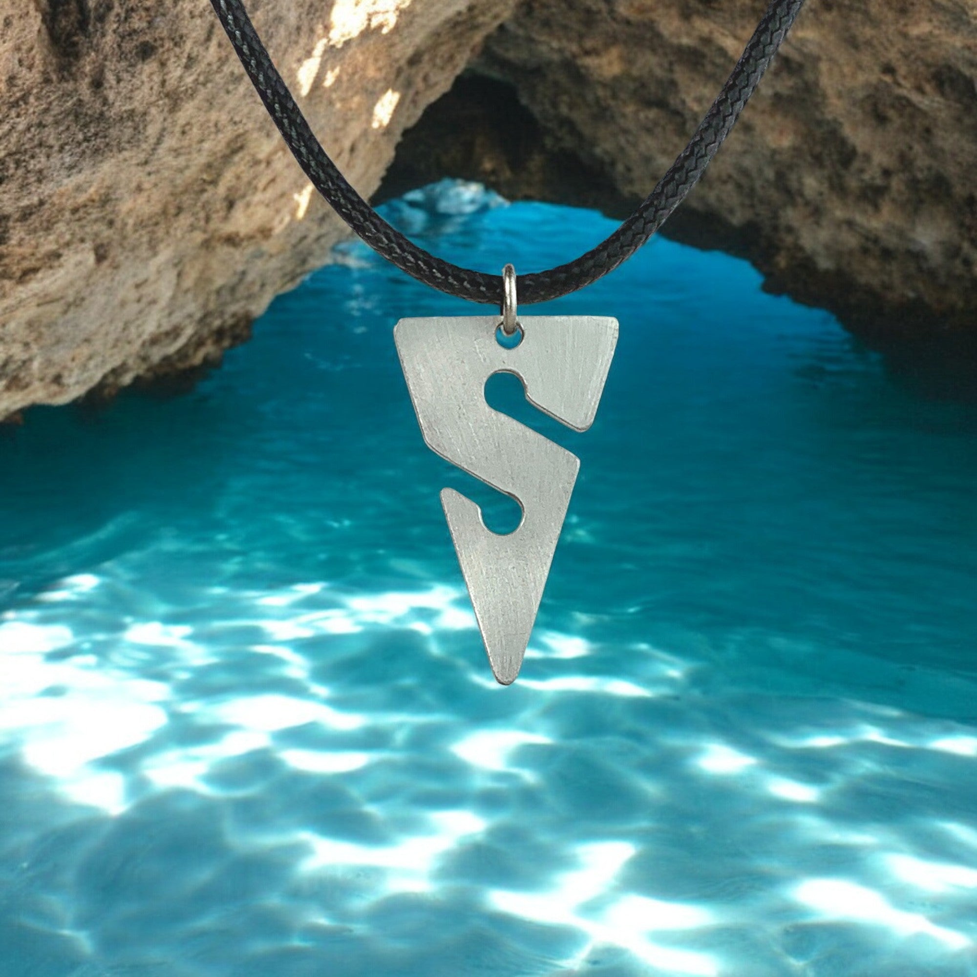 Silver pendant on a black cord against a natural rock and water background