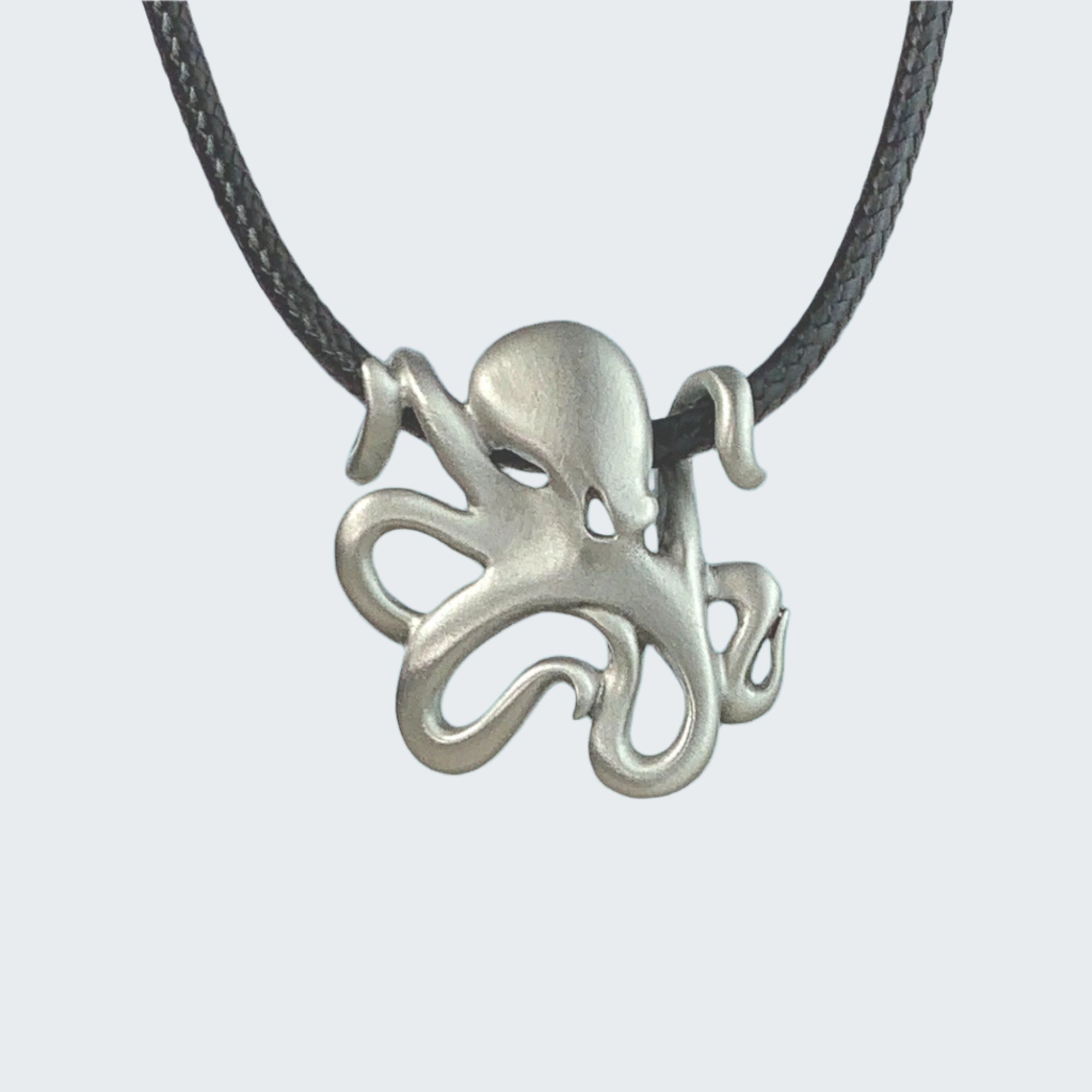 Silver octopus pendant on a black cord with a beach and ocean background