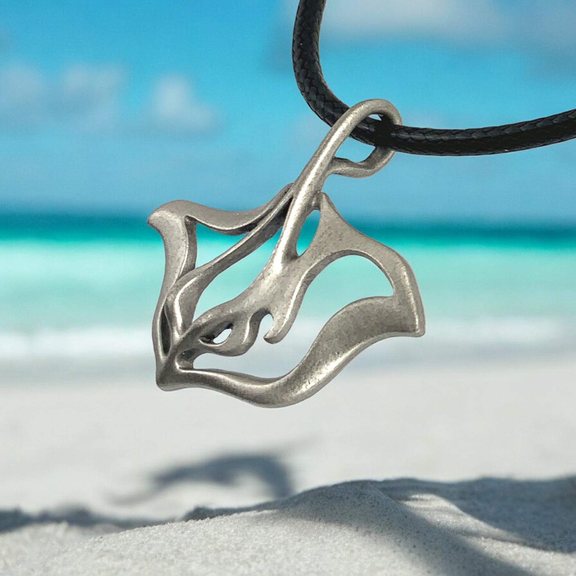 Silver pendant on a black cord with a beach and ocean background