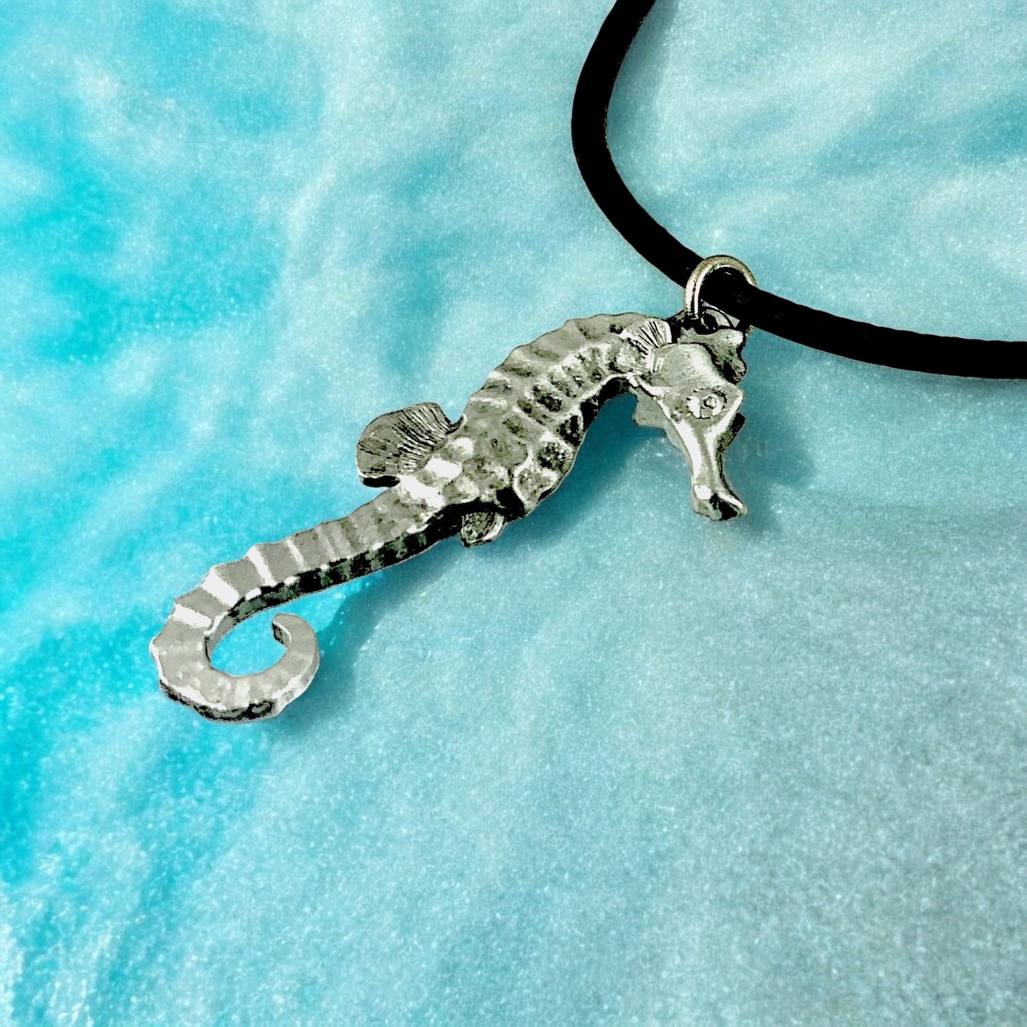 Silver seahorse pendant on a black cord against a blue textured background