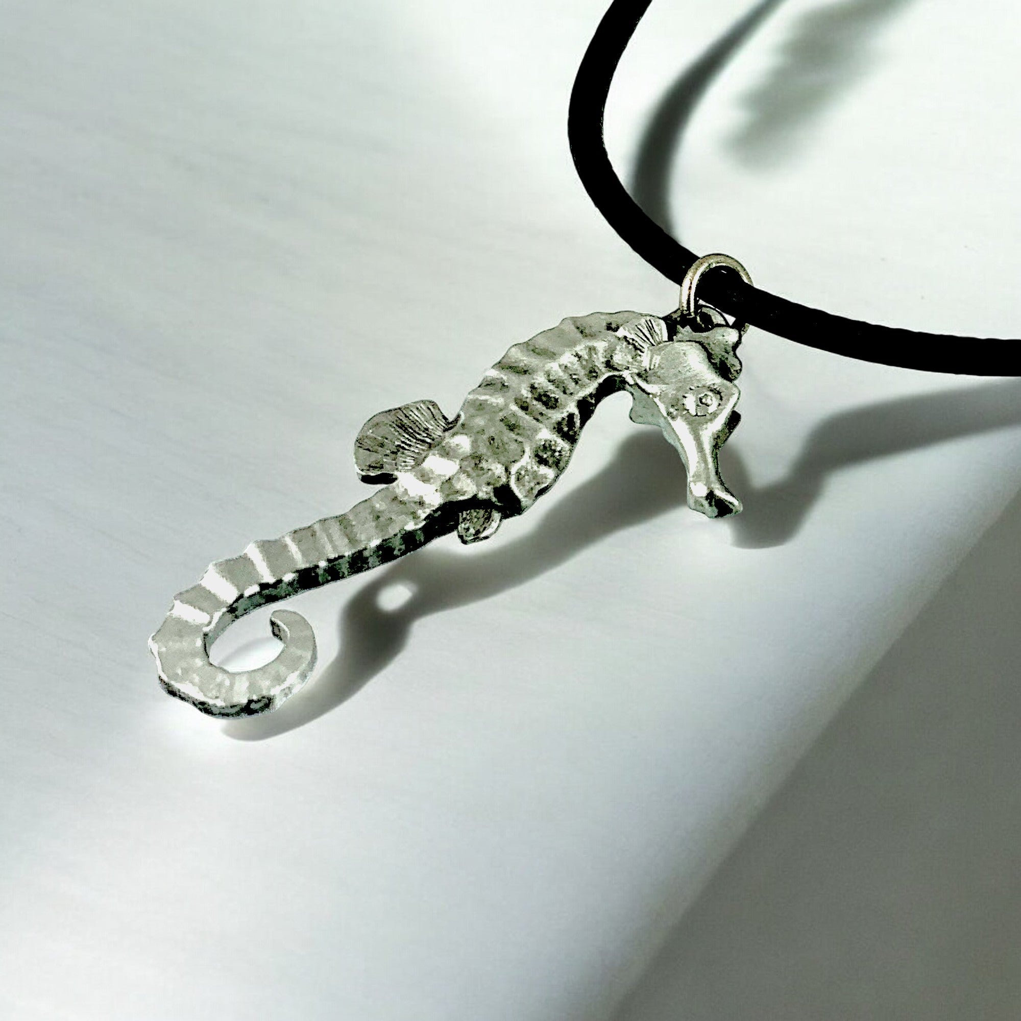 Silver seahorse pendant on a black cord against a white background