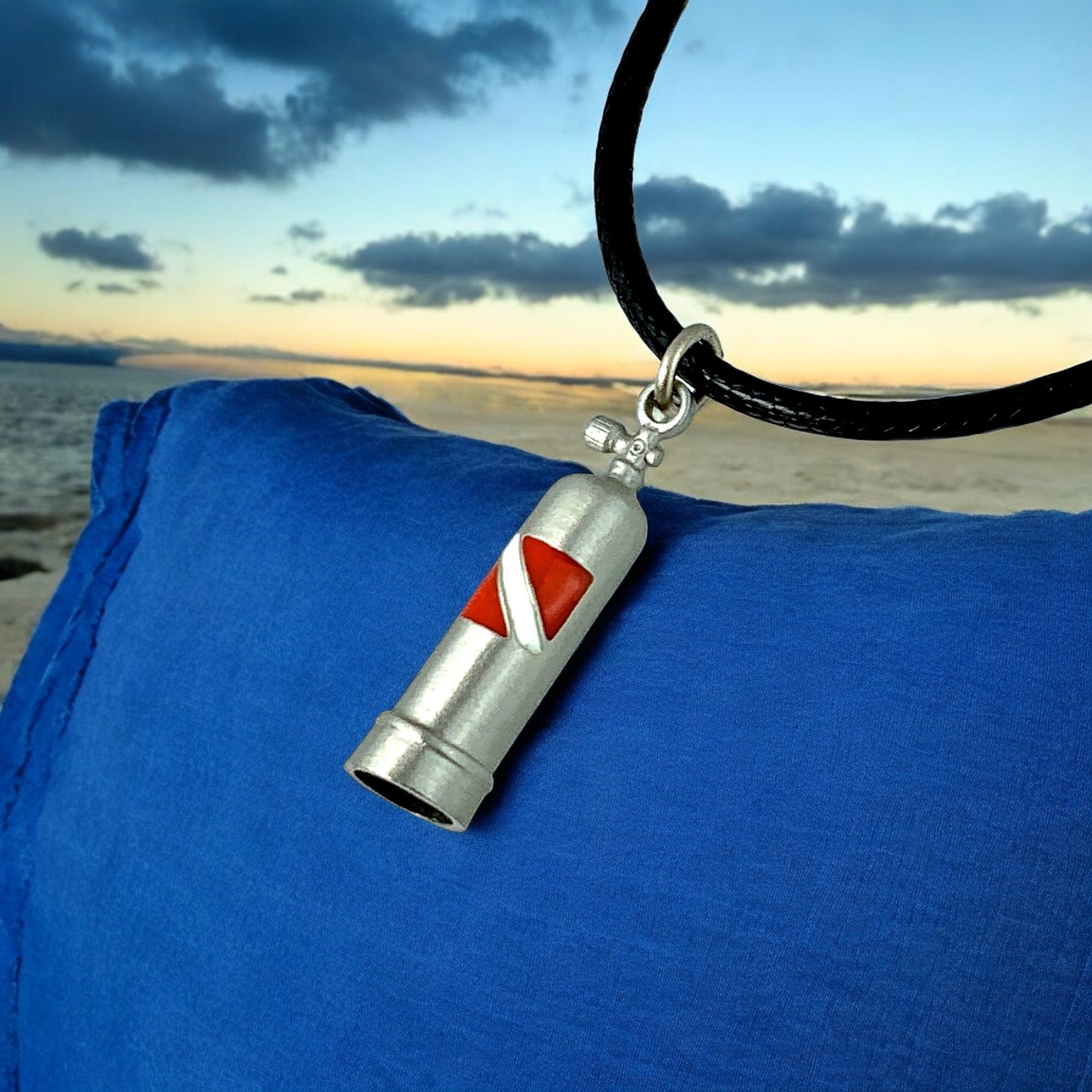 Silver whistle pendant with red center on a black cord against a blue fabric background