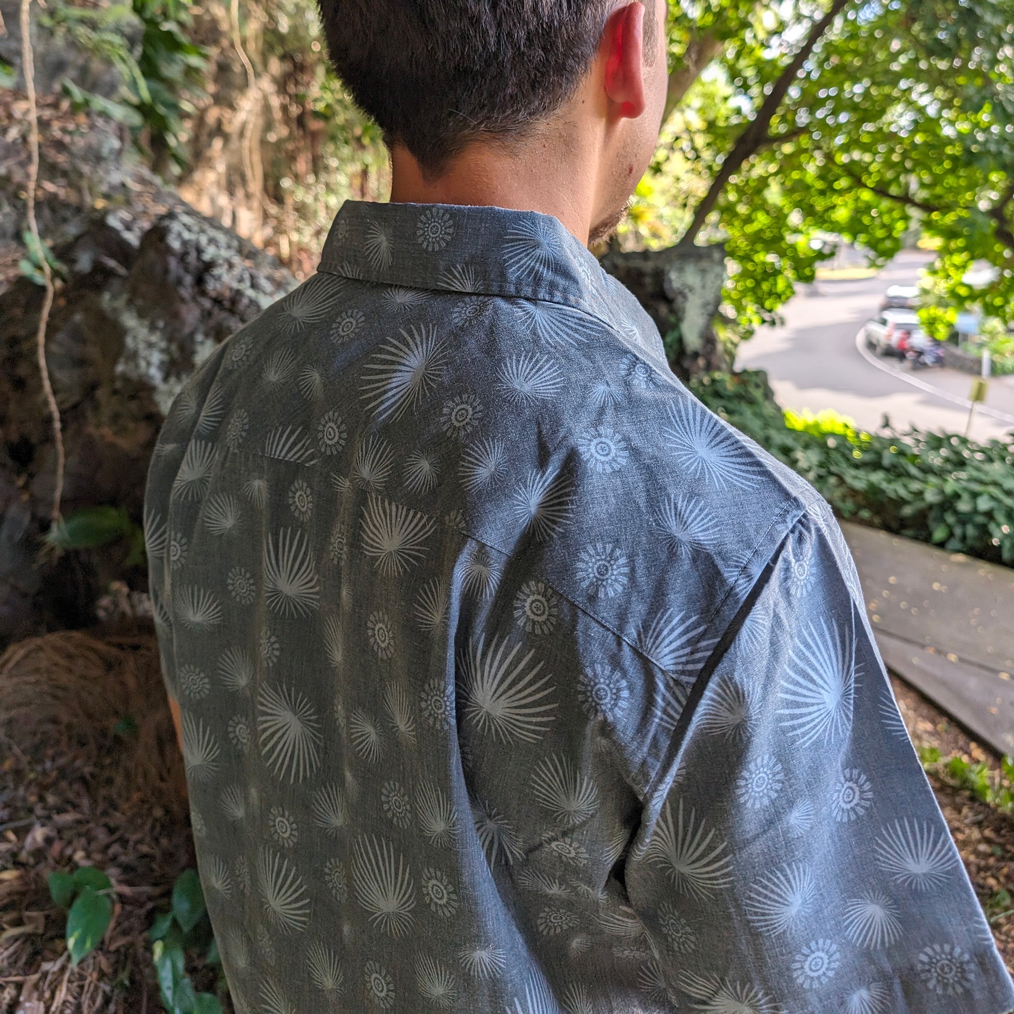 Person wearing a dark blue patterned shirt outdoors with greenery in the background