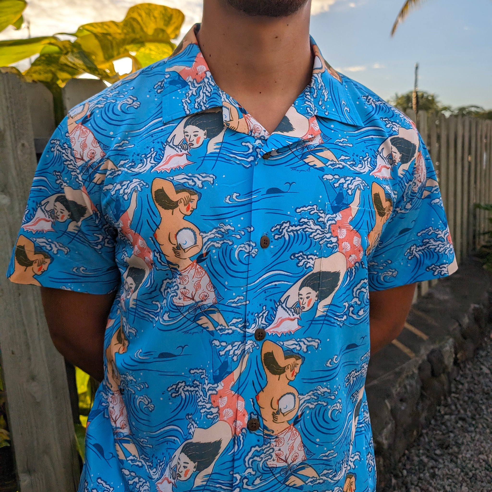Person wearing a blue Hawaiian shirt with cartoon mermaid design outdoors.