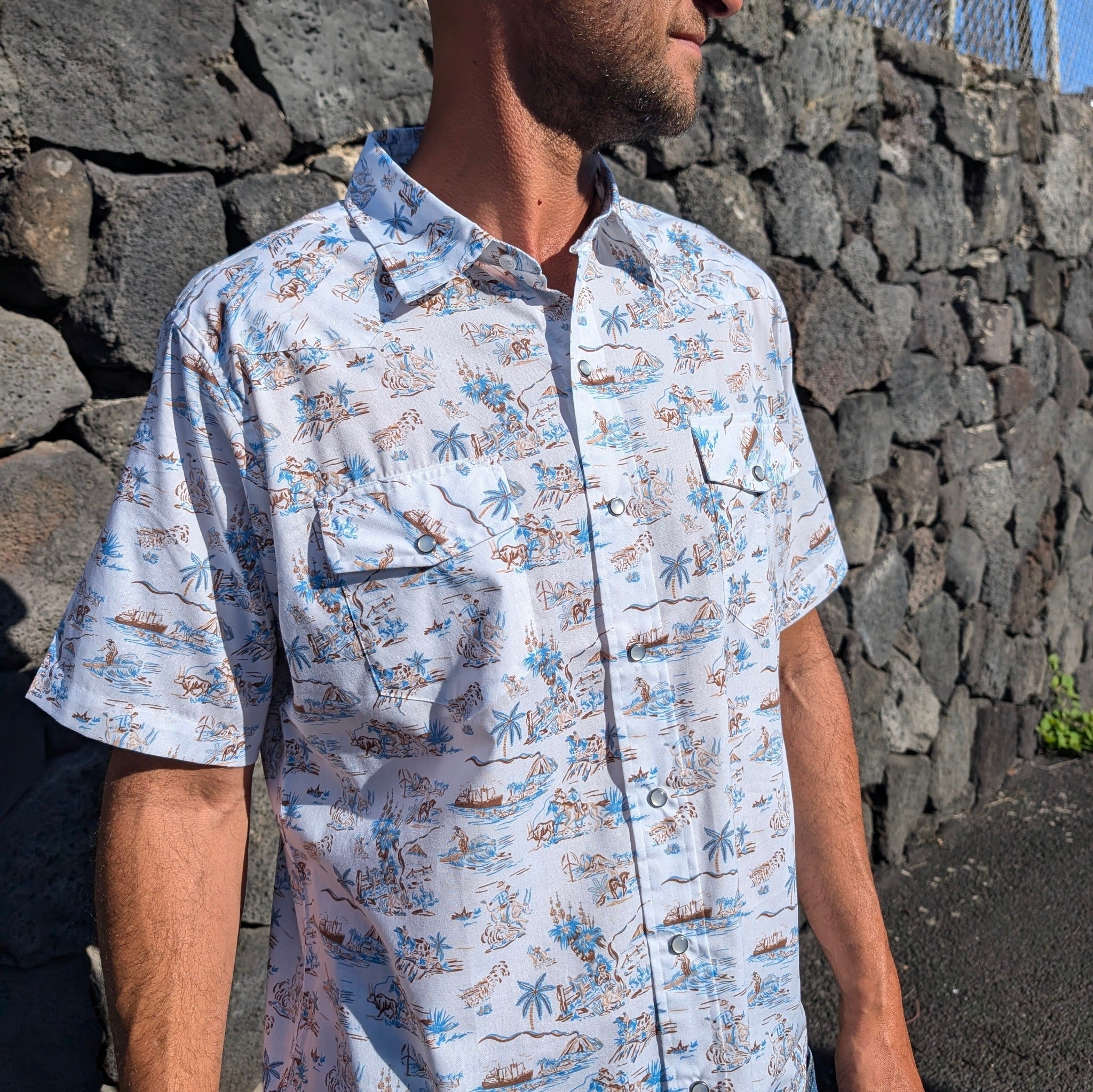 Person wearing a patterned shirt standing against a stone wall.
