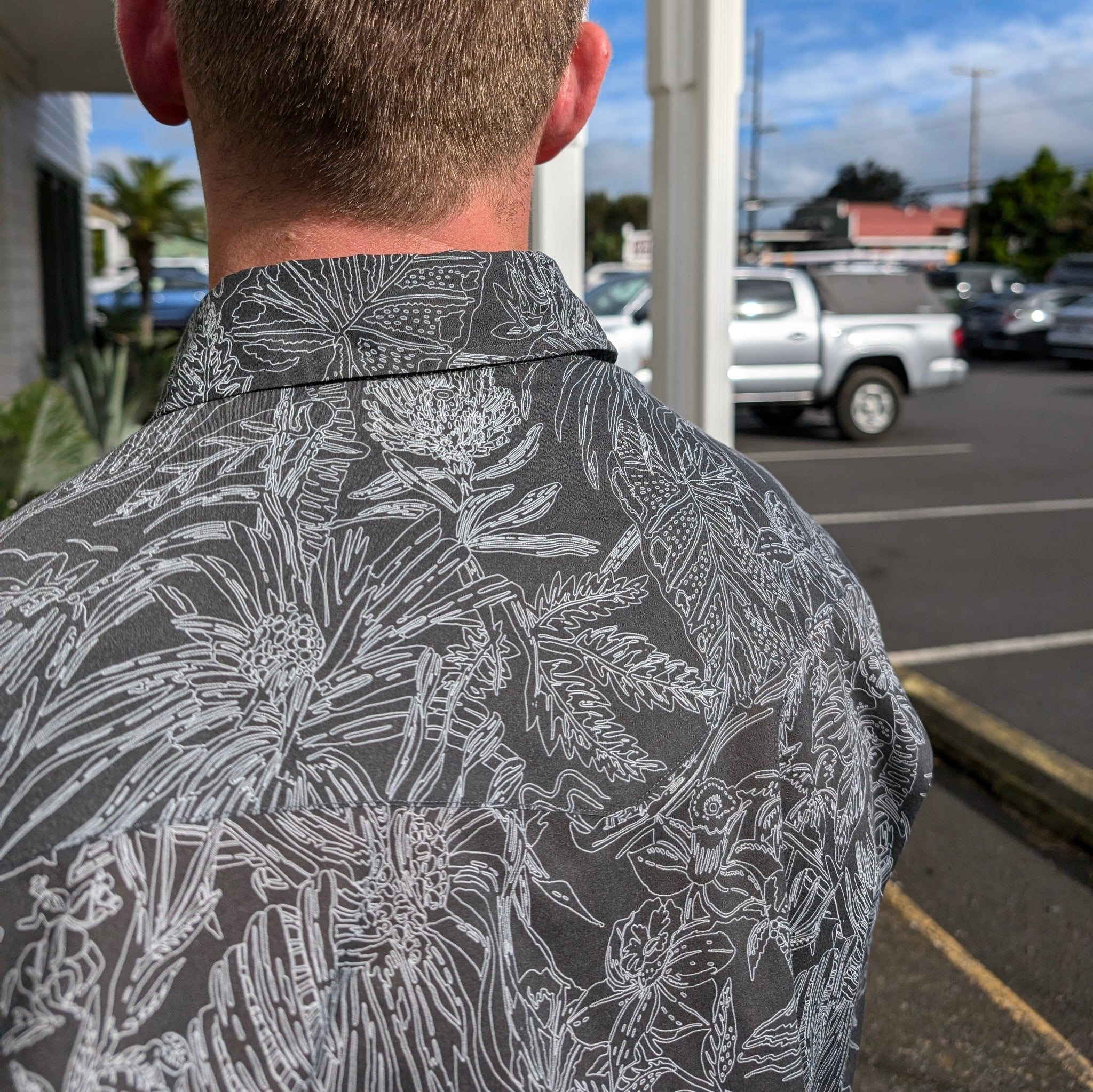 Person wearing a gray floral patterned shirt in a parking lot.