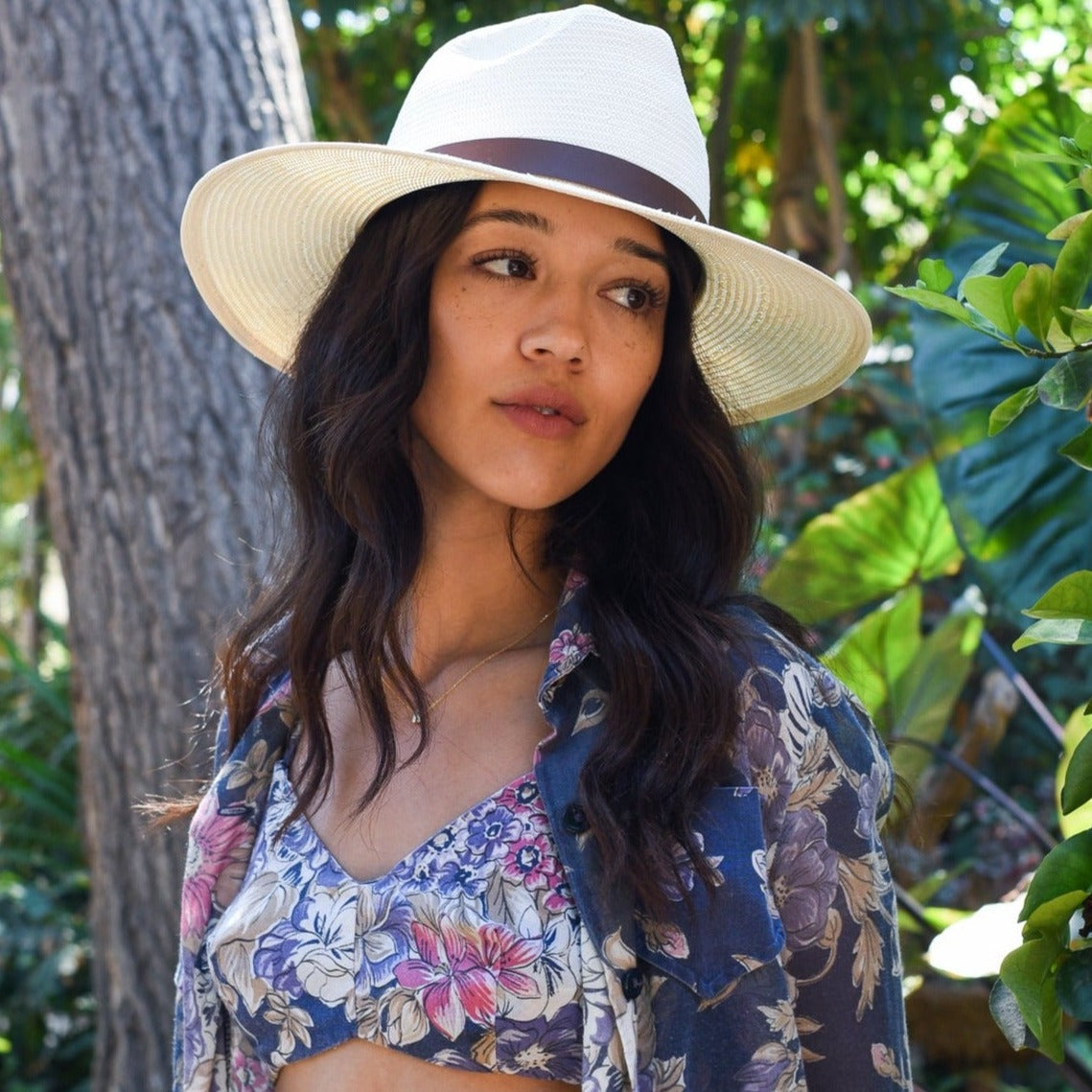 Woman wearing a wide-brimmed hat in a natural setting with greenery.