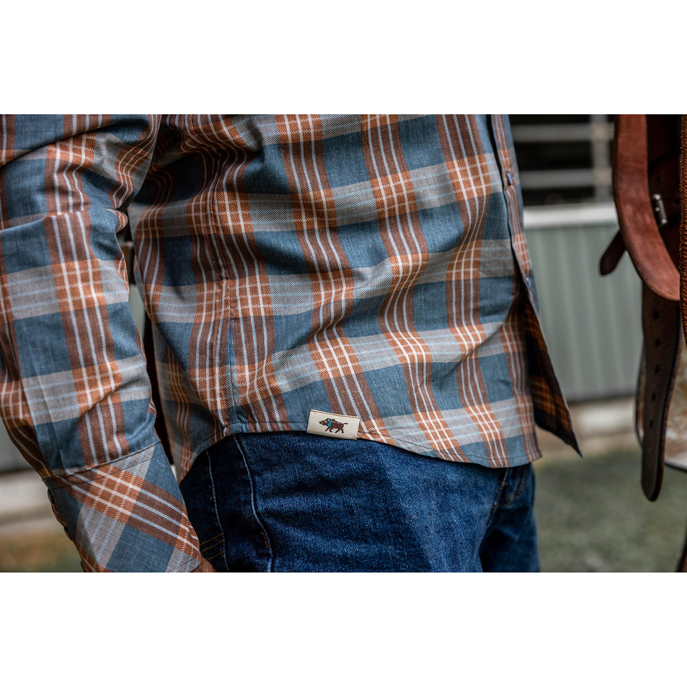 Plaid shirt with a visible brand logo worn by a person, with a blurred background.