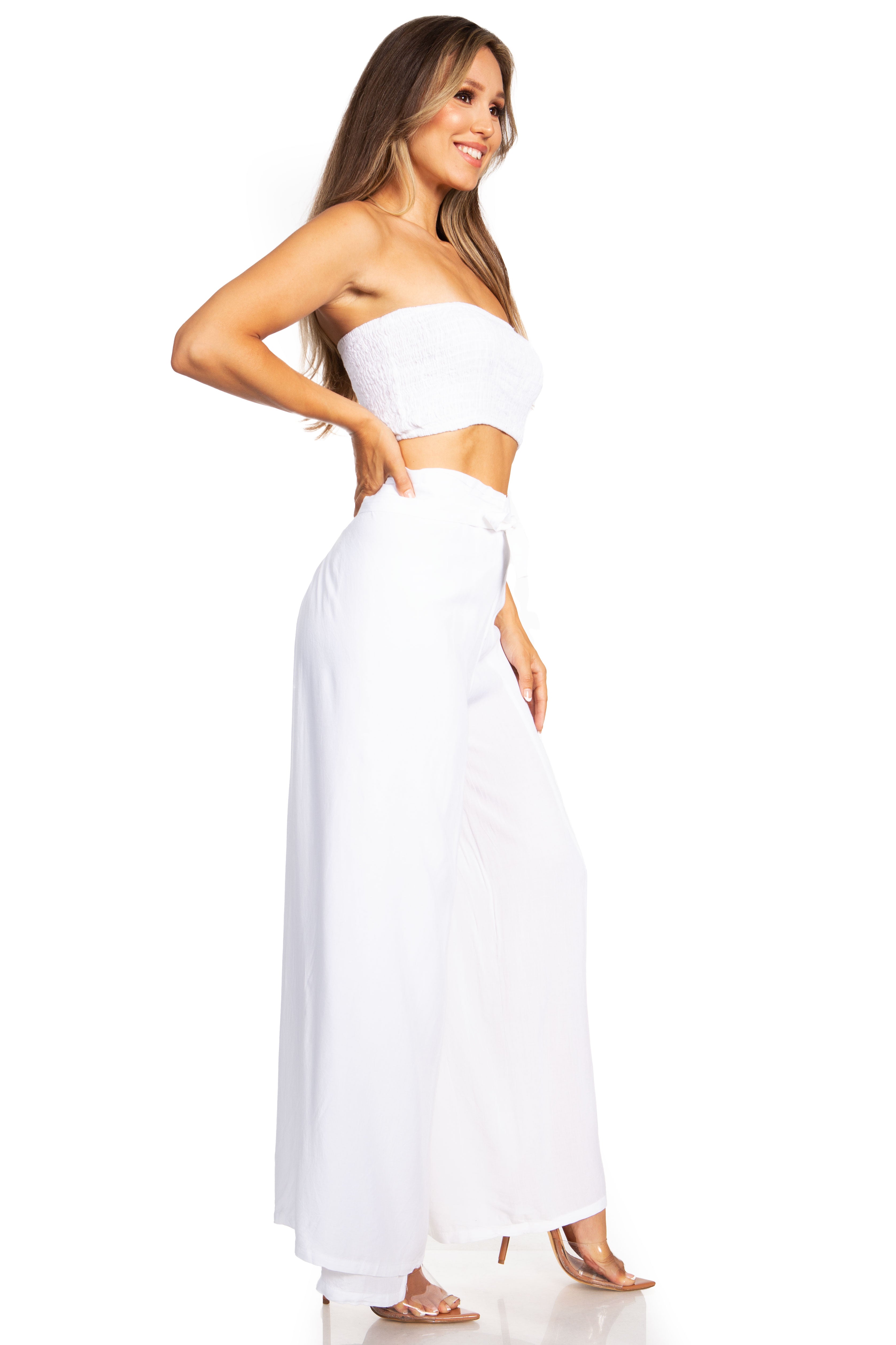 Woman wearing a white strapless top and long white pants on a white background