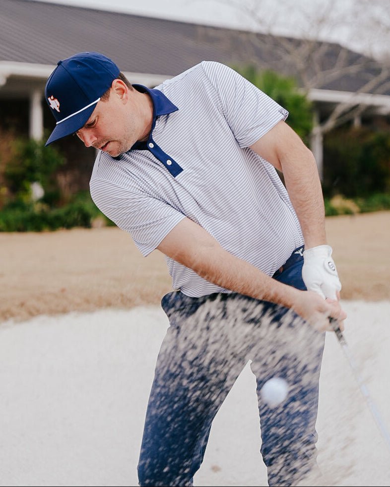 Man playing golf in a sand trap wearing a cap and striped shirt.