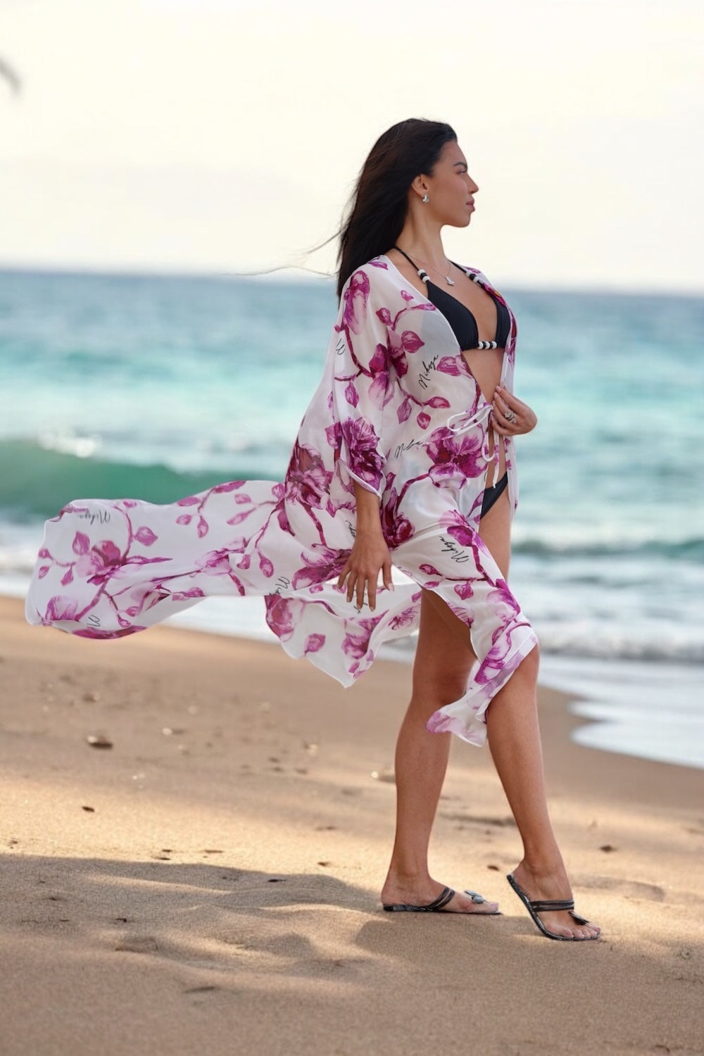 Woman in a floral kimono walking on a beach with ocean in the background