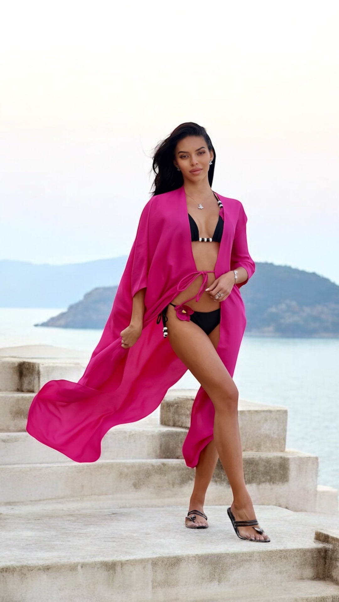 Woman in a pink cover-up standing on steps by a body of water with mountains in the background.