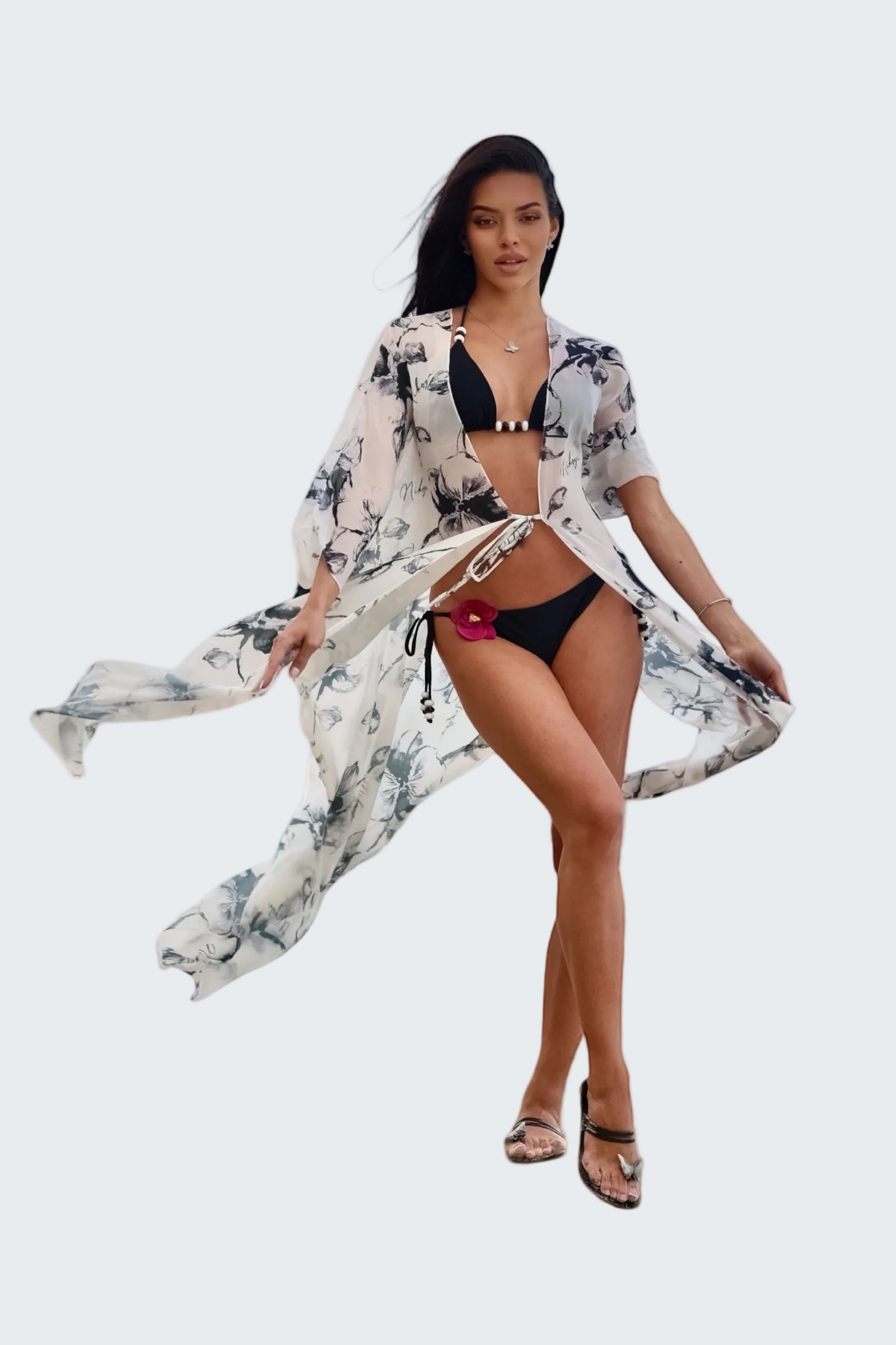 Woman in a black bikini with a floral cover-up standing on a stone ledge with a scenic background.