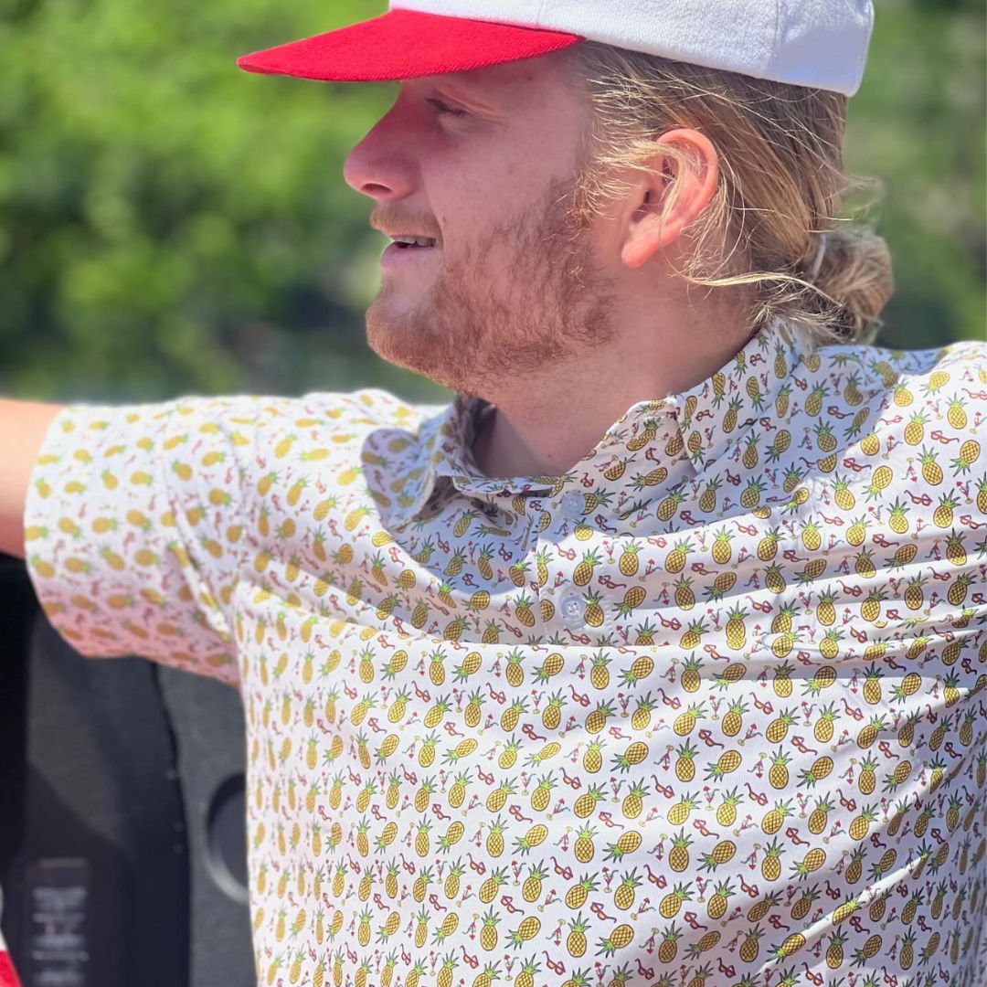 Person wearing a patterned shirt with a hood, red cap, and white cap outdoors.
