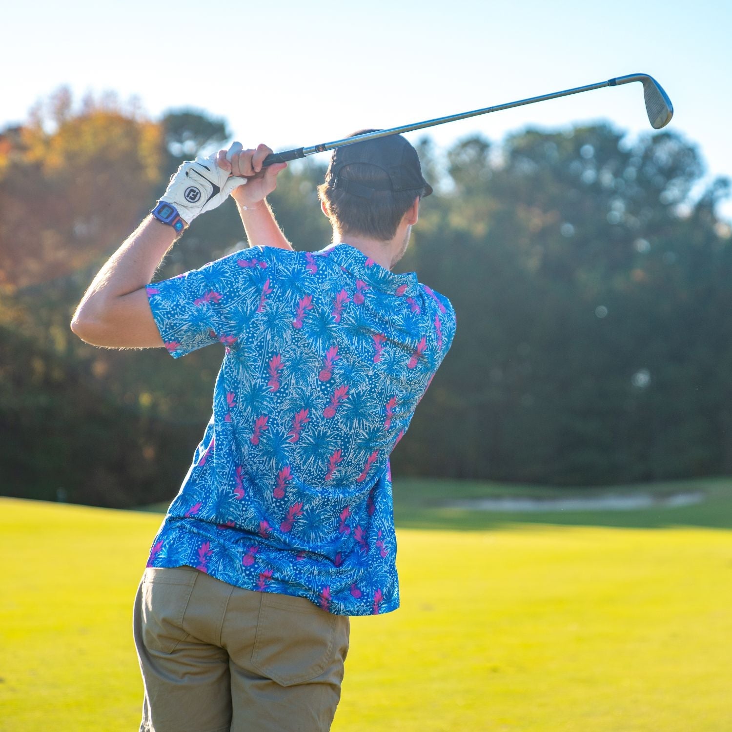 Person playing golf on a sunny day with trees in the background