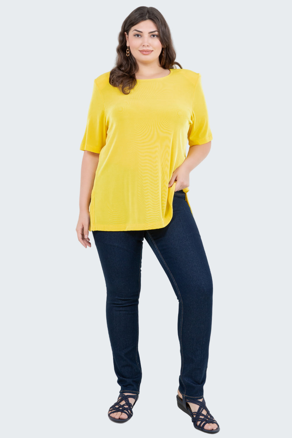 Woman wearing a yellow top and dark blue jeans on a white background