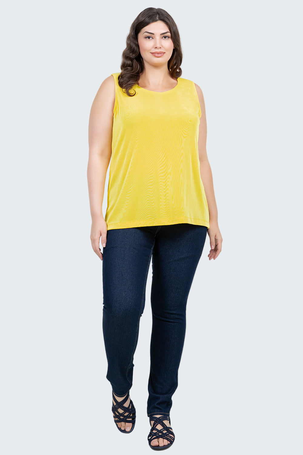 Woman wearing a yellow sleeveless top and dark blue jeans on a white background