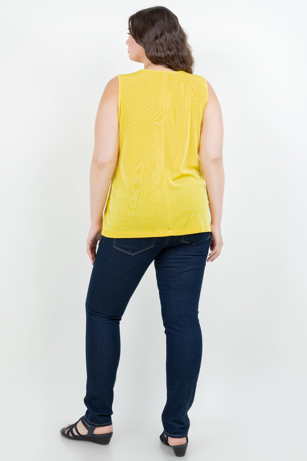 Woman wearing a yellow sleeveless top and blue jeans on a white background