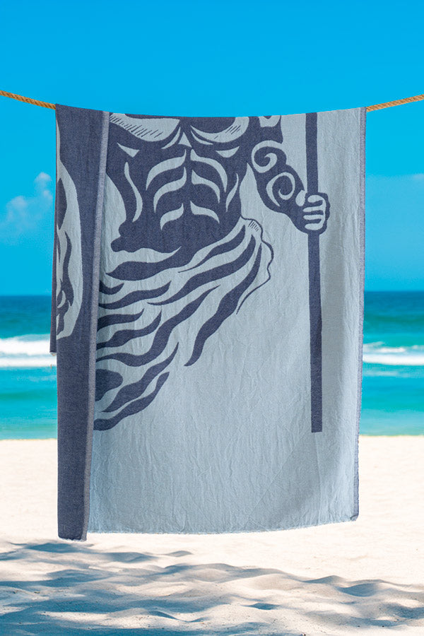 Towel with a design of a person holding a shell on a beach with blue sky and ocean.