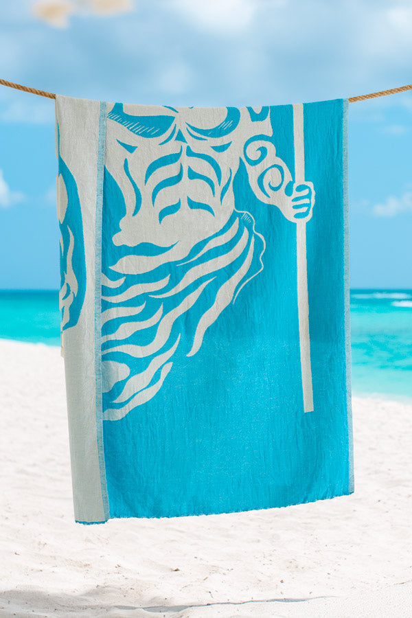 Turquoise beach towel with white design on a beach with ocean and sky in the background