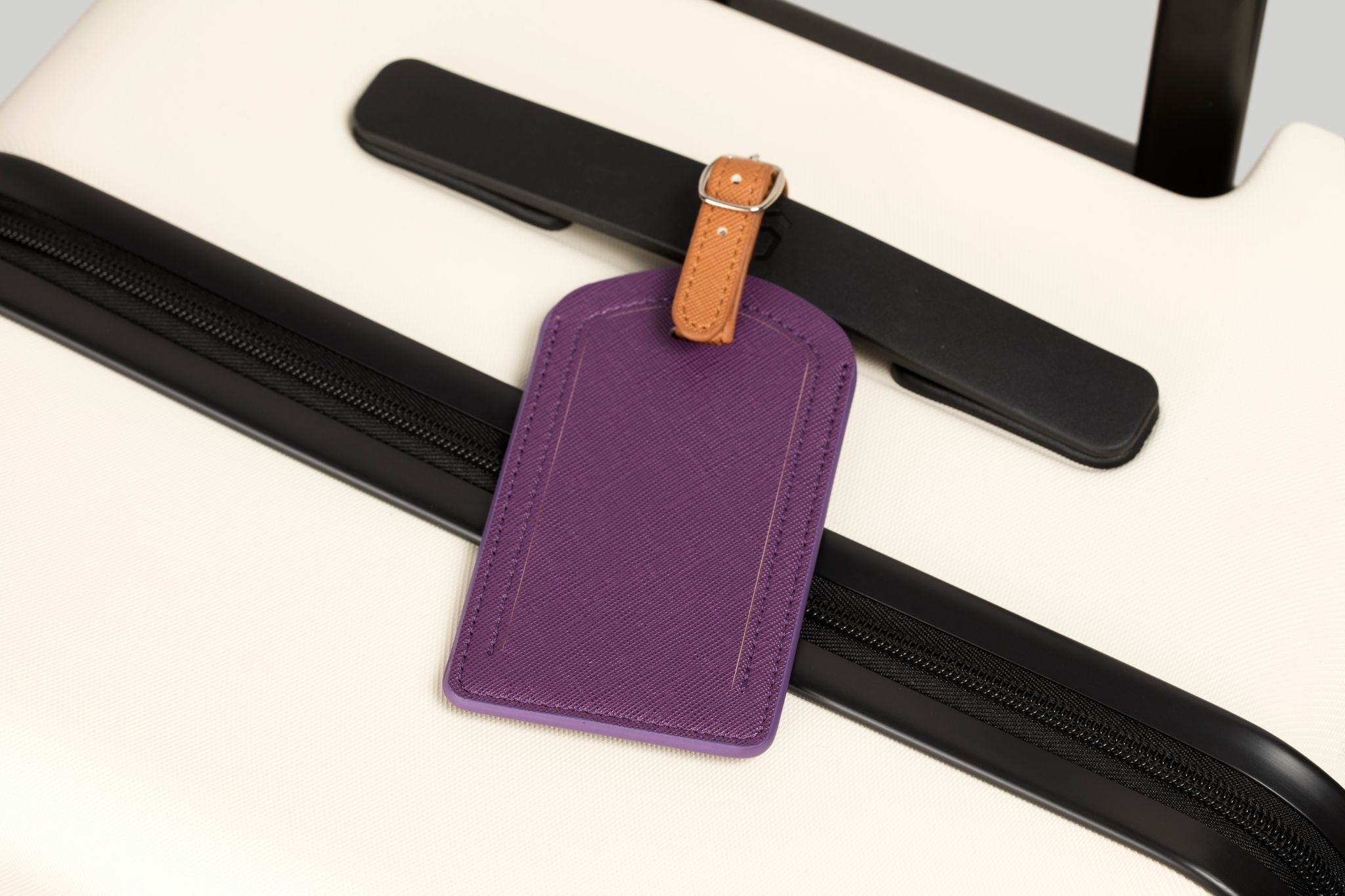Purple luggage tag with brown strap attached to a suitcase handle.