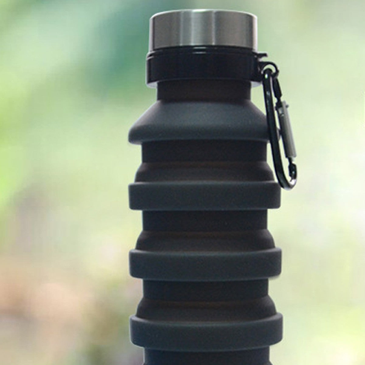 Collapsible black water bottle with metal cap on a blurred green background