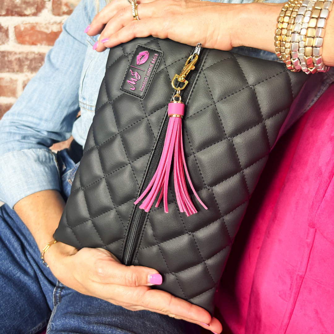 Person holding a black quilted clutch with a pink tassel and keychain.