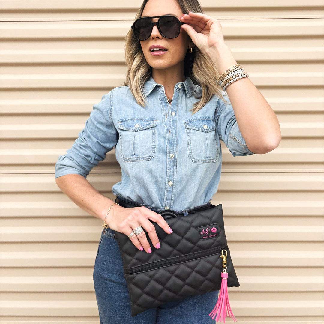 Woman wearing a denim shirt and sunglasses, holding a black quilted clutch with a pink tassel.