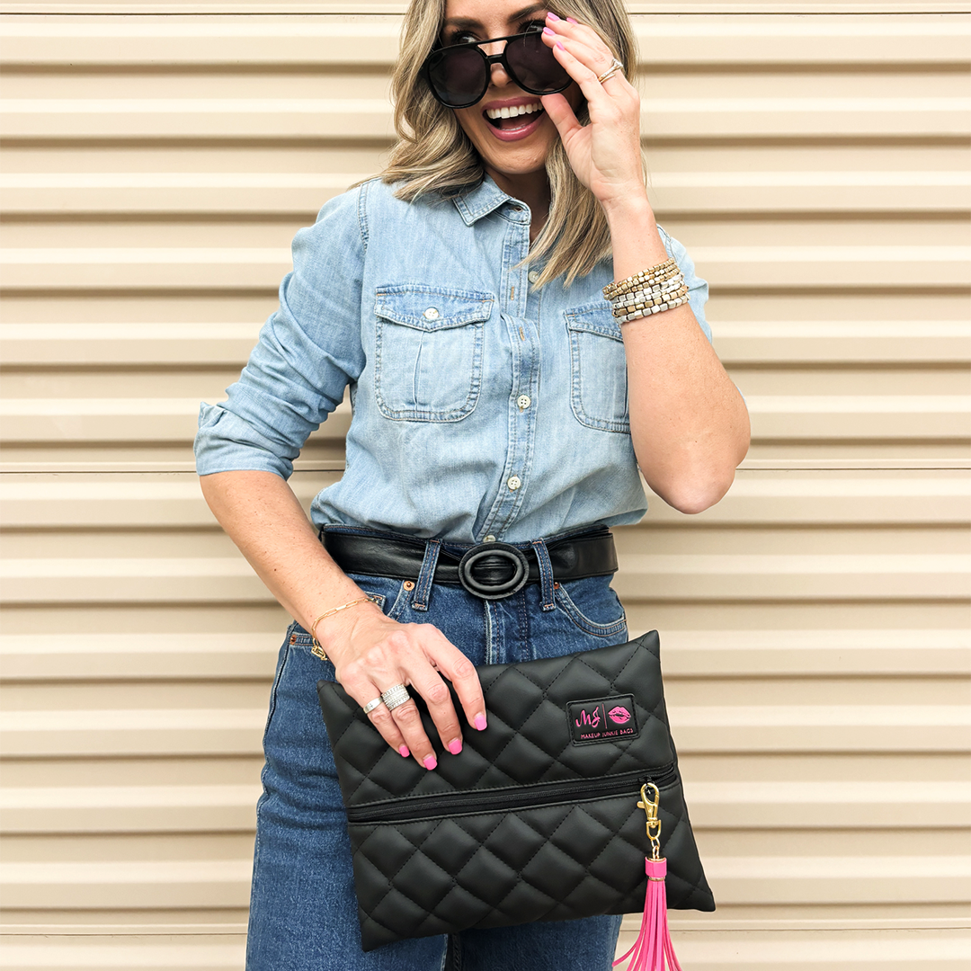 Woman holding a black quilted handbag with a visible brand logo against a beige background