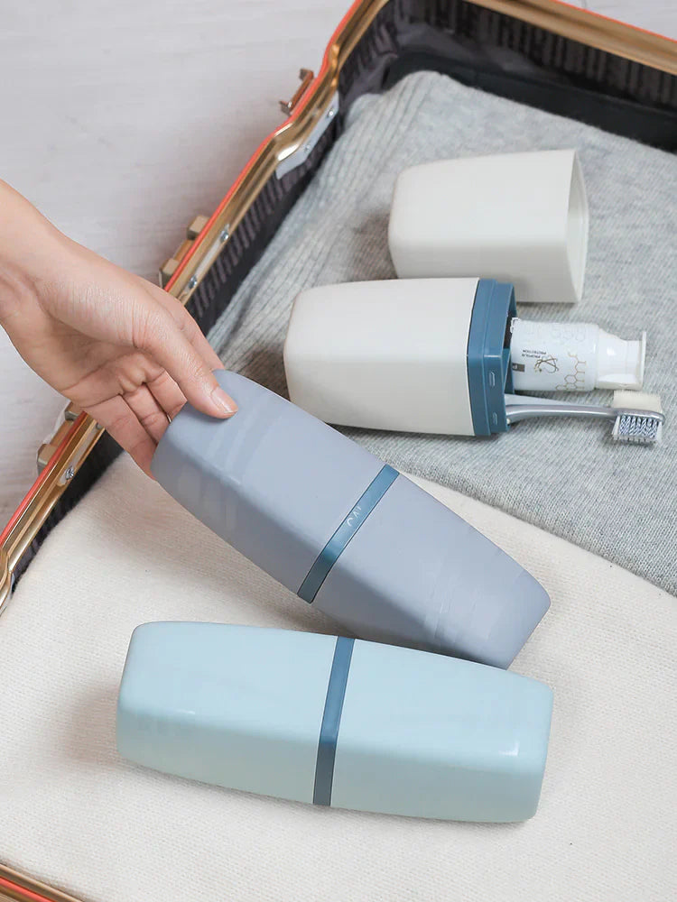 Two travel-sized toothbrushes in blue and gray containers on a suitcase with gray fabric lining.