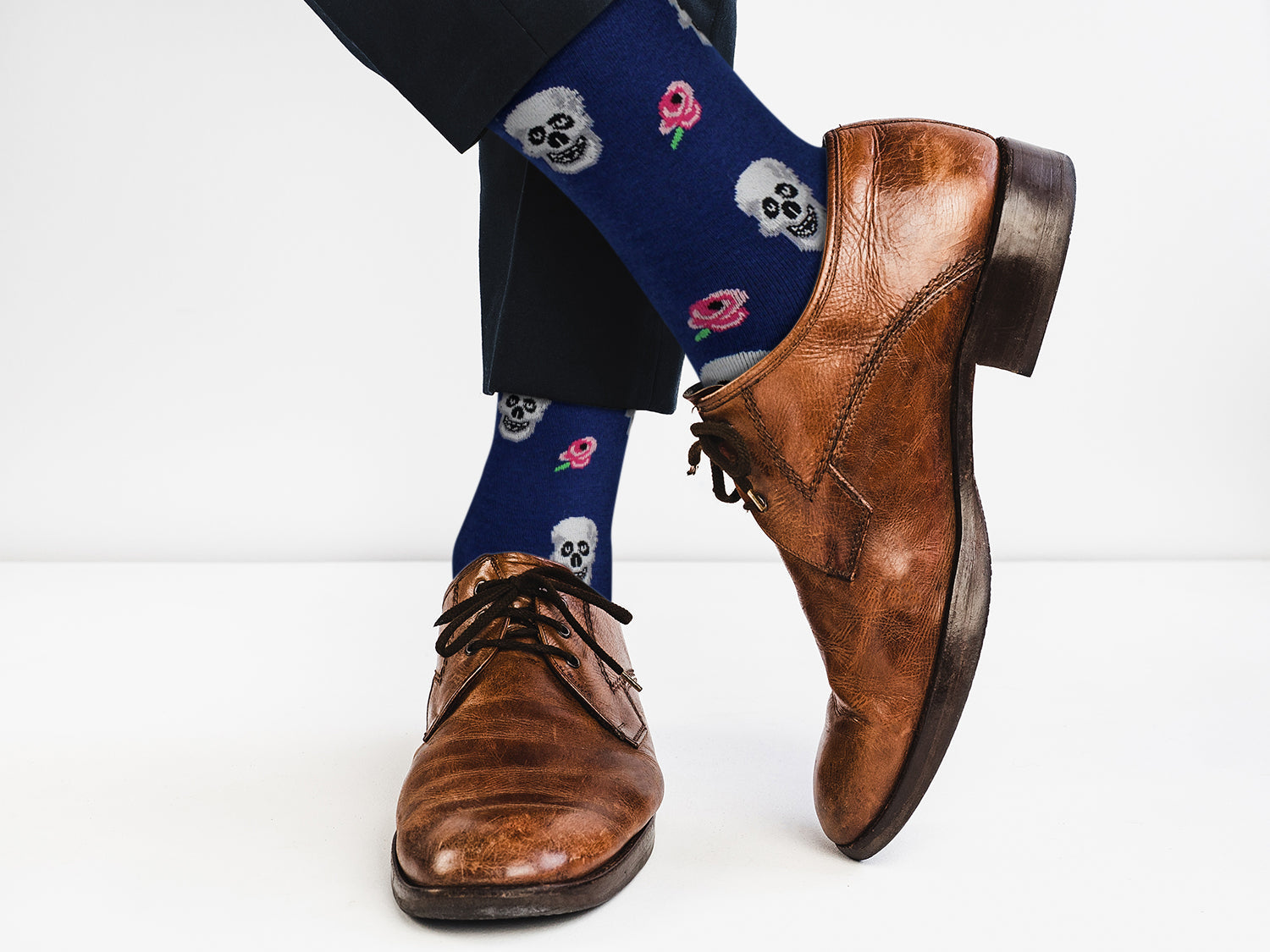 Brown leather shoes with blue socks featuring skull and rose designs on a white background