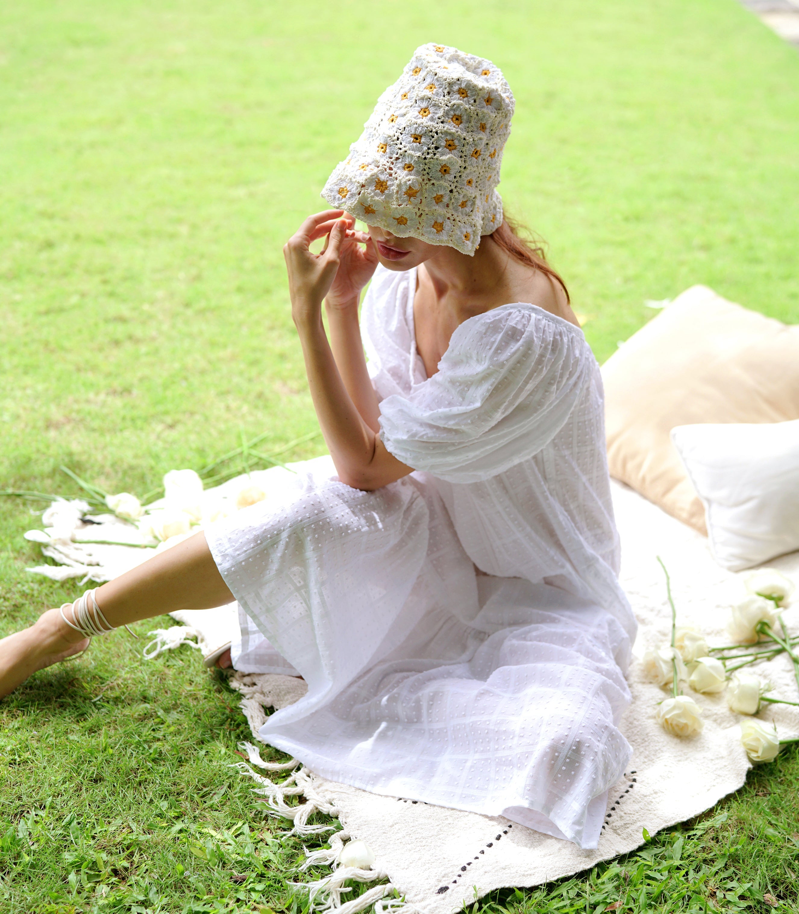 Woman in a white dress sitting on grass with a floral headscarf