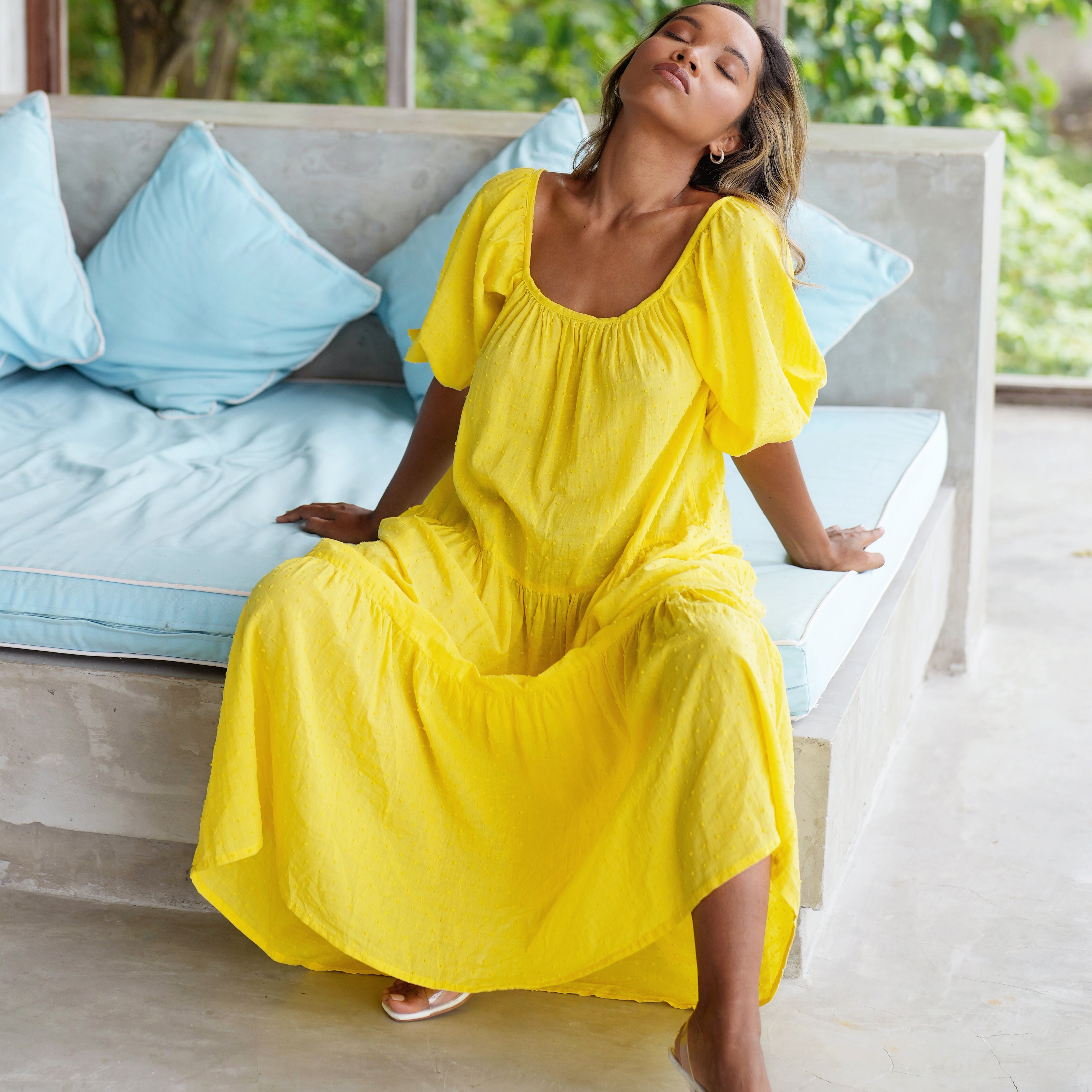 Woman in a yellow dress sitting on a couch with blue pillows.