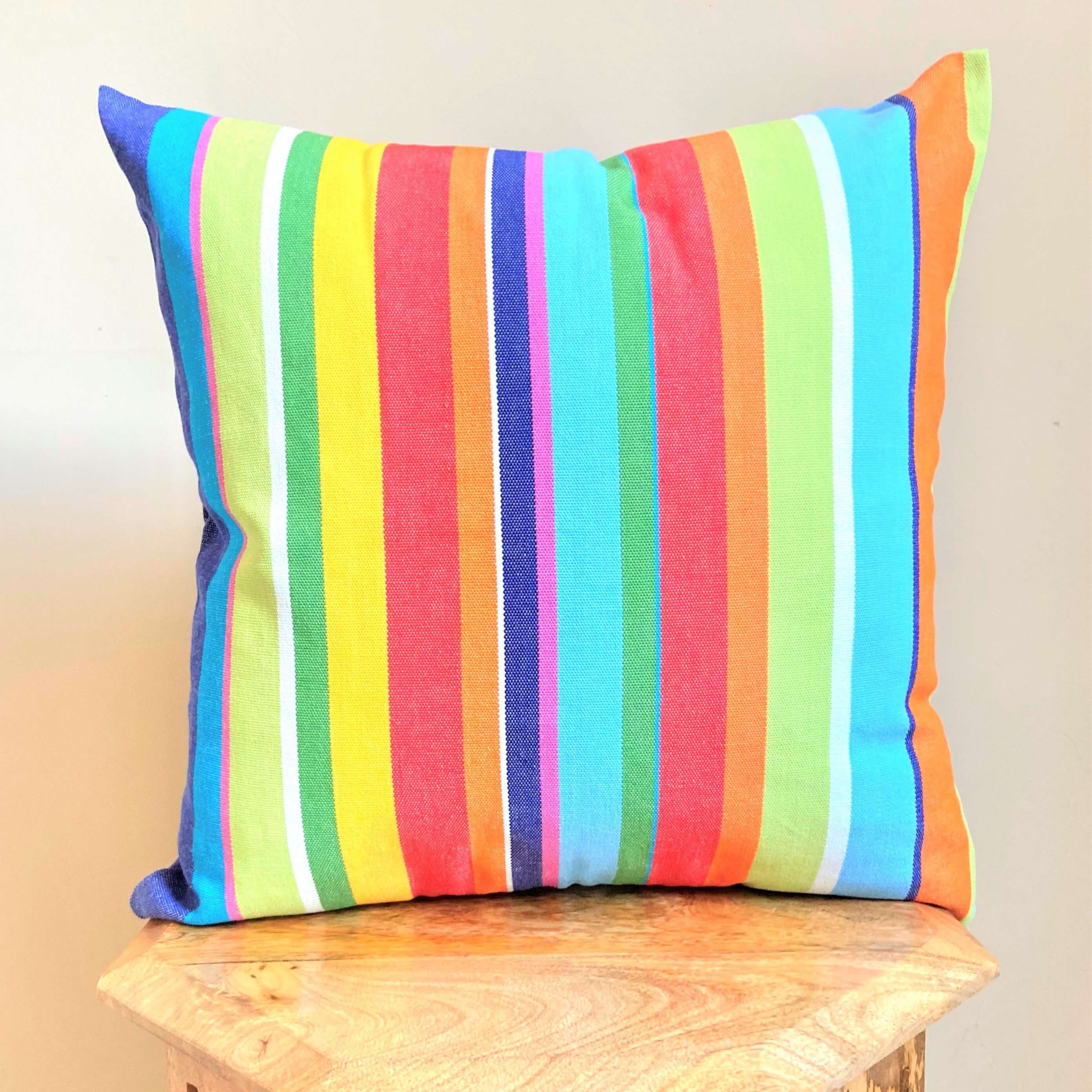 Colorful striped pillow on a wooden stool against a beige background