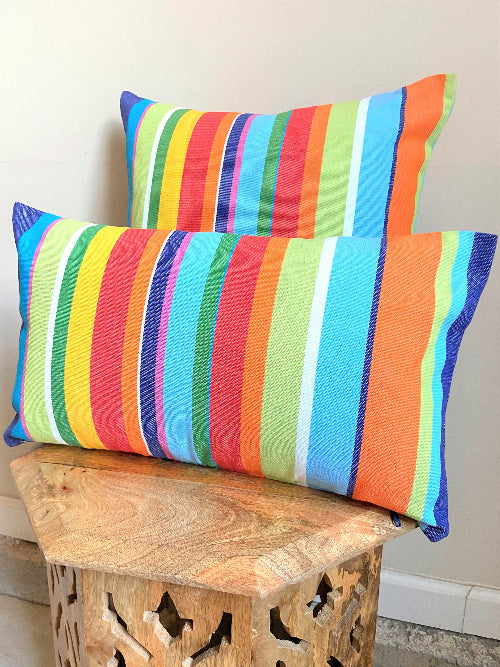 Two colorful striped pillows on a wooden bench against a neutral wall.