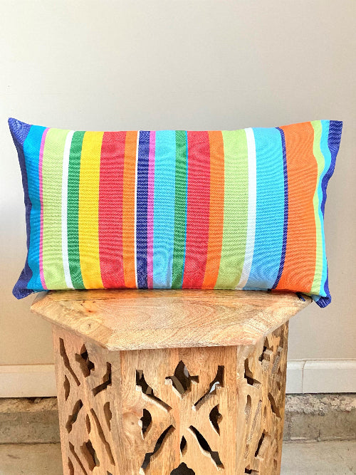 Colorful striped pillow on a wooden stool against a plain wall