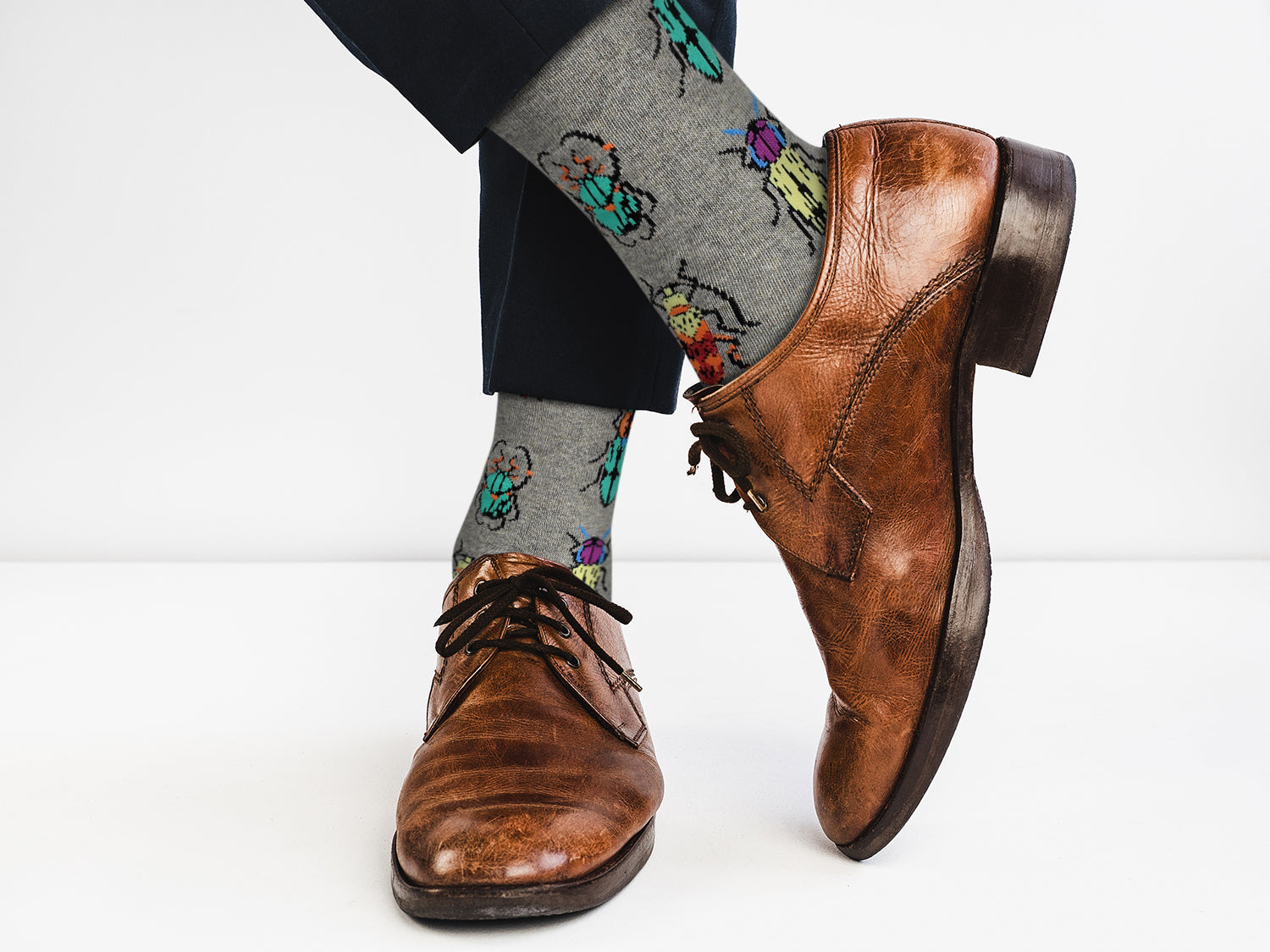 Brown dress shoes with gray socks featuring colorful beetle designs on a white background