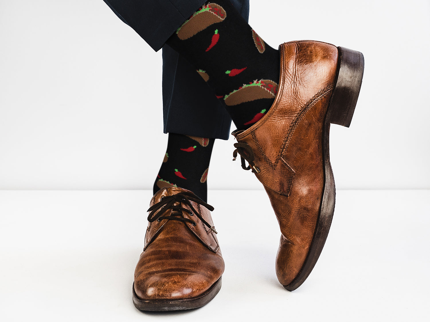 Brown leather shoes worn with black pants featuring food-themed socks on a white background