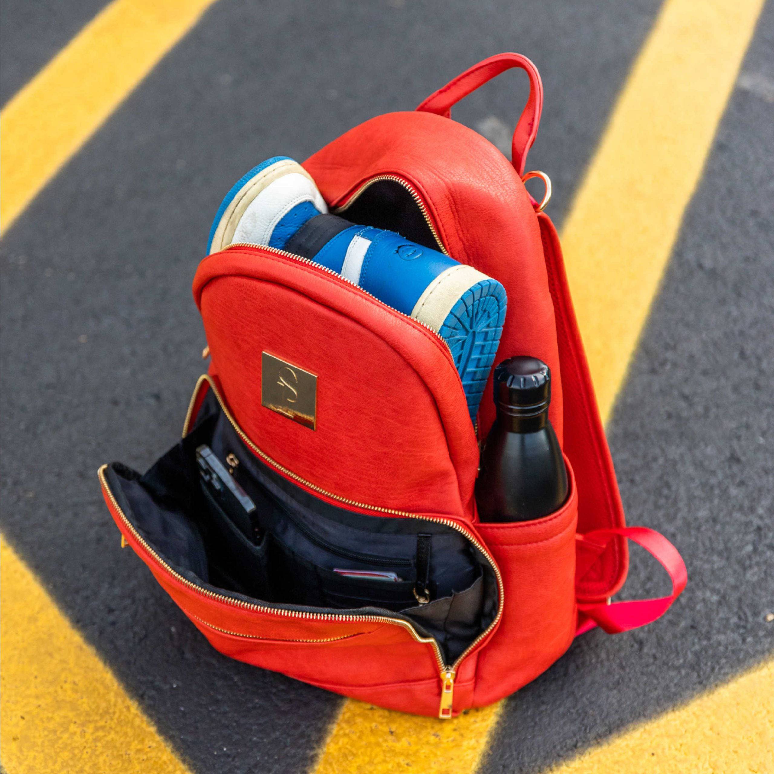 Red backpack with shoes and a bottle on a road surface