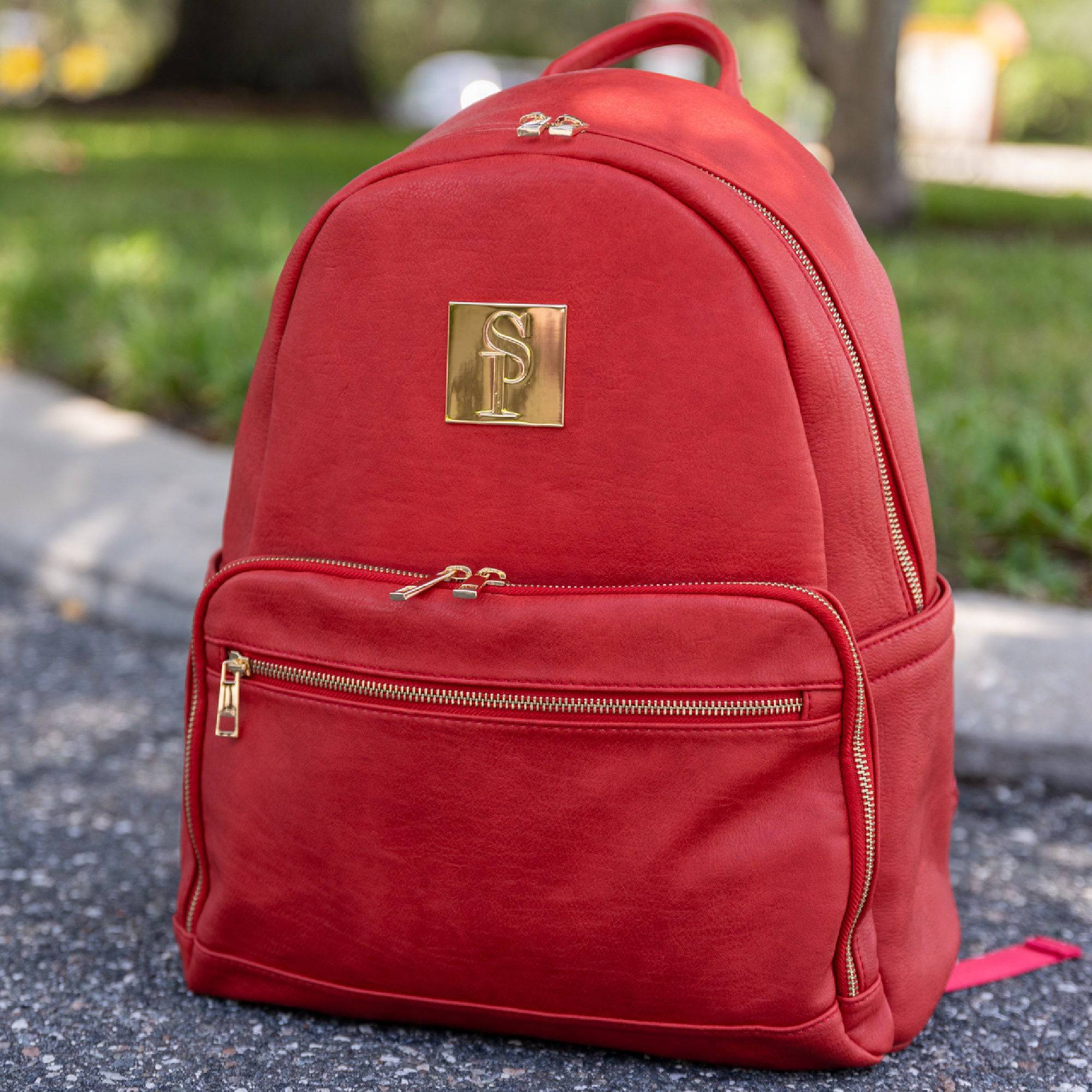 Red backpack with a gold logo on a blurred outdoor background